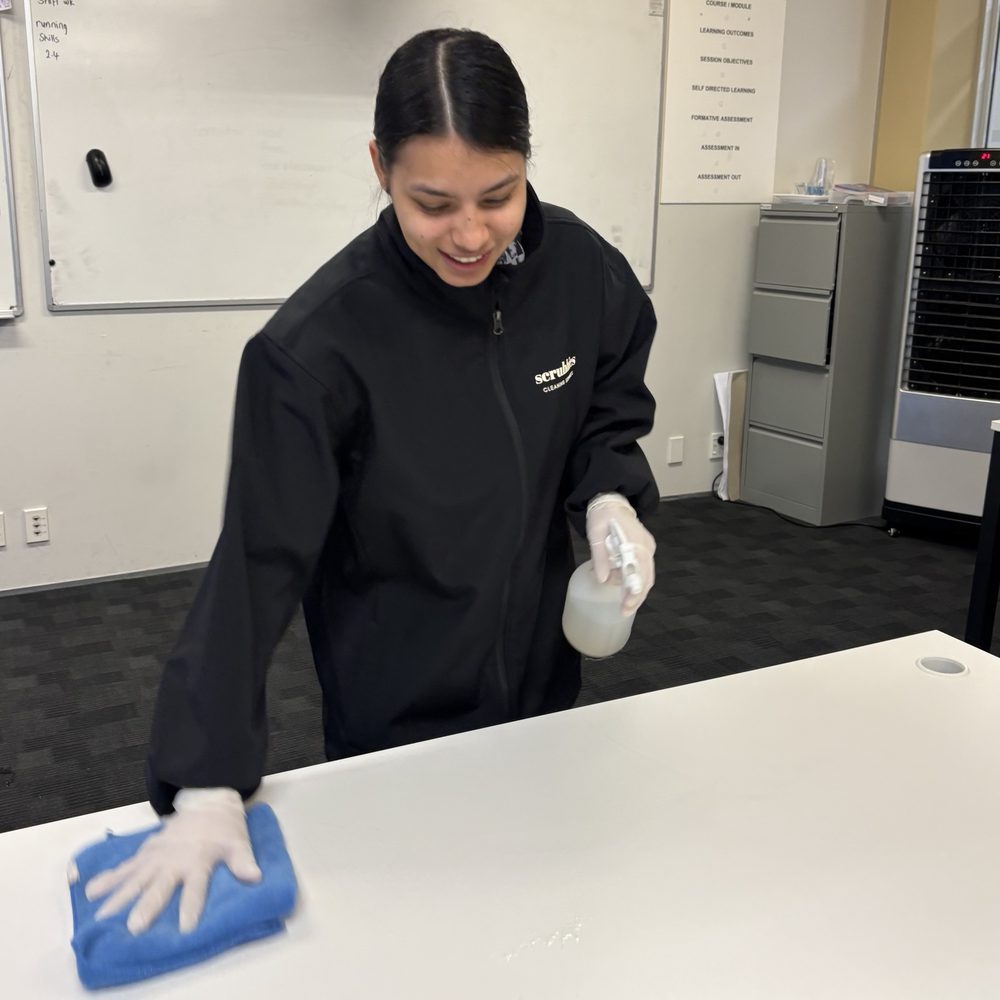 Scrubbies cleaner laughing while wiping down a classroom desk