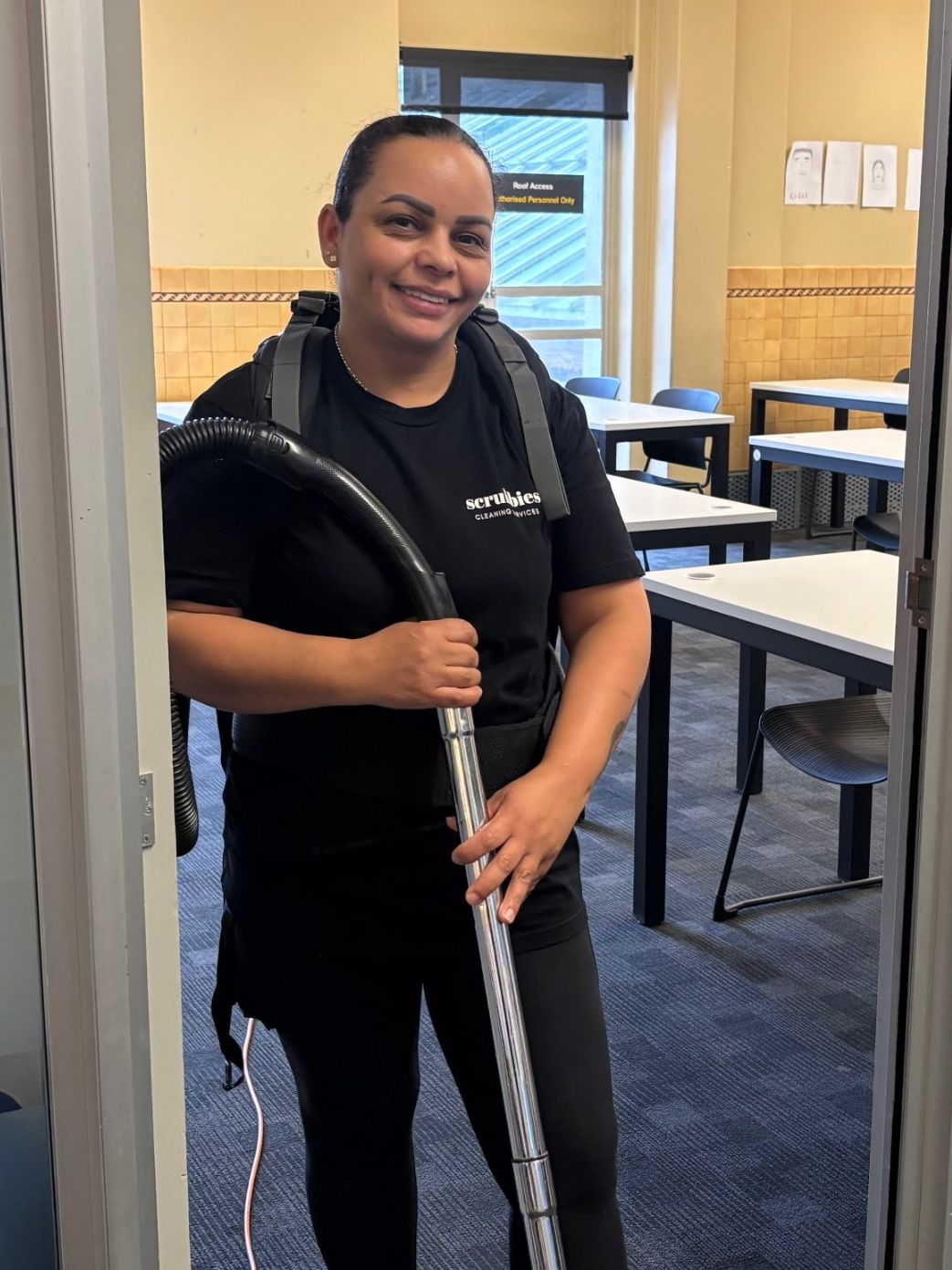 Smiling Scrubbies cleaner vacuuming a classroom
