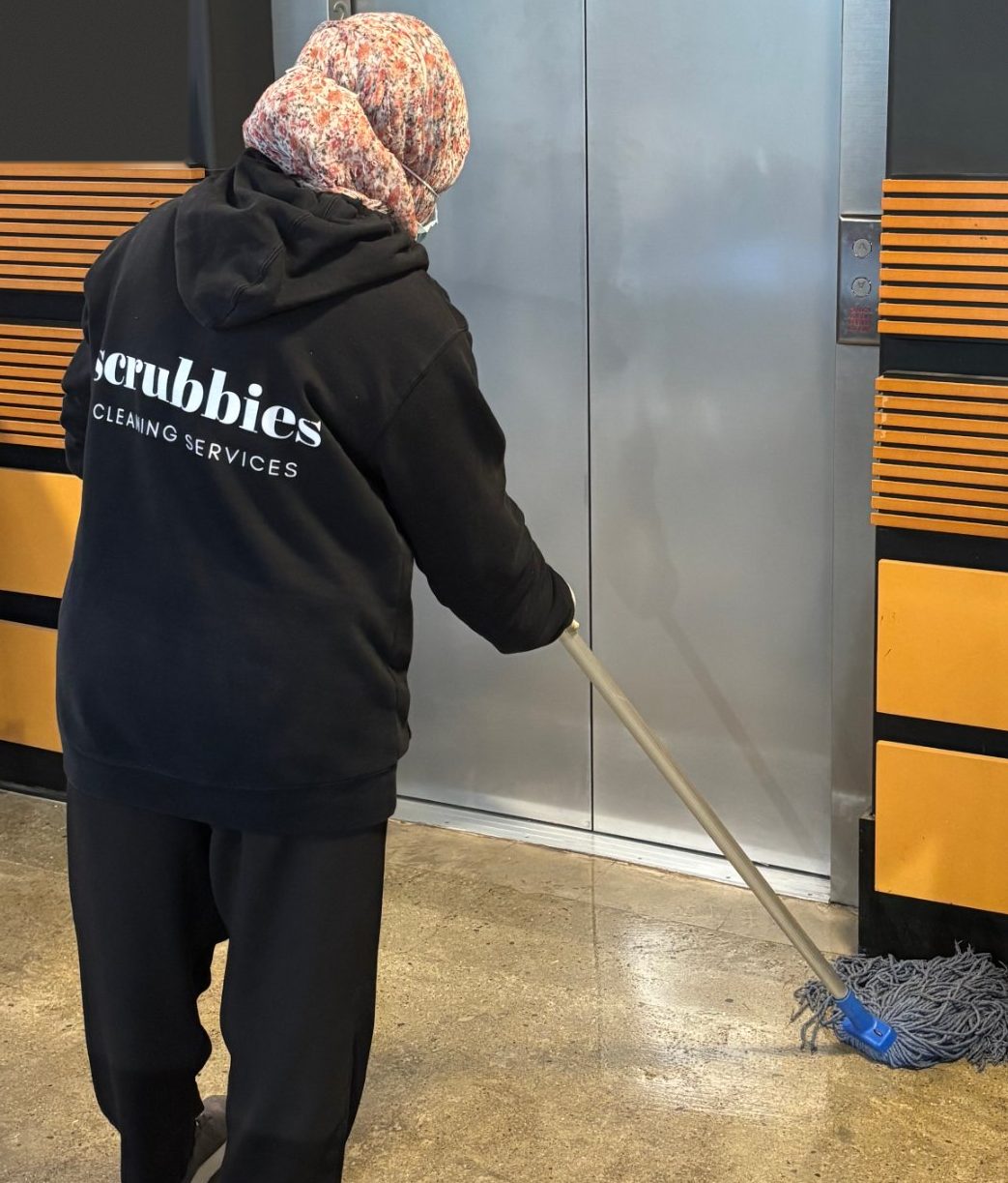 Scrubbies cleaner in a branded hoodie mopping outside a lift