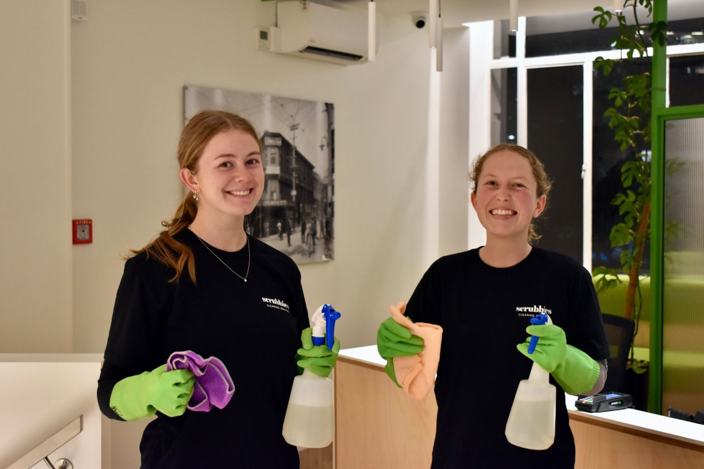 Two smiling Scrubbies cleaners at a reception desk